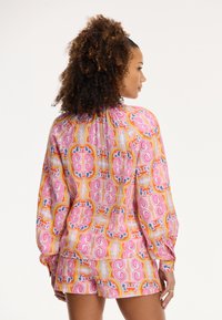 Ilgām piedurknēm blūze ar elastīgām aprocēm un saskaņotiem šortiem. Raksts satur rozā, oranžā un zilā krāsā ziedu elementus uz viegla auduma.