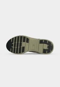 Semelle de chaussure en caoutchouc vert olive avec des patins de traction noirs, comportant plusieurs rainures horizontales pour l'adhérence et la flexibilité.