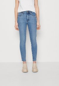 Jeans ajustados de color azul claro hechos de denim, con una cintura alta, cierre de botón y un ligero desgastado, combinados con zapatos slip-on beige.