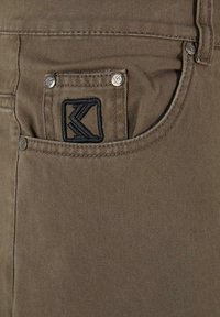 Khaki denim jeans med en tekstureret overflade, der har et syet logo på baglommen og metalnitter til forstærkning.