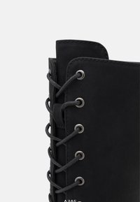 Botte noire à lacets avec tige en cuir lisse, œillets métalliques et coutures renforcées le long du bord pour plus de durabilité.