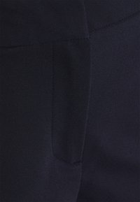 Gros plan d'un tissu bleu marine foncé avec des coutures visibles et un détail de poche sur un vêtement.
