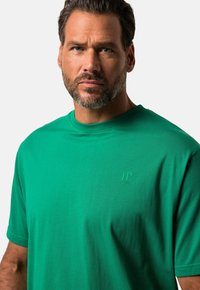 T-shirt verde in cotone con scollatura a girocollo, maniche corte e logo in rilievo sul petto. Tessuto liscio e vestibilità casual.