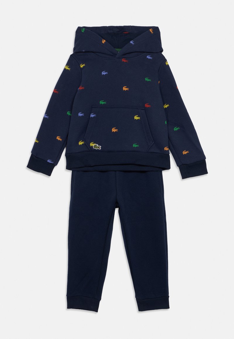 Tumši zila kapucīna krekla un bikses komplekts ar daudzkrāsainām izšūtām krokodila emblēmām, kas izkaisītas pa krekla virsmu.