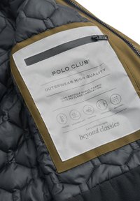 Tkanina z pikowanego ciemnoszarego materiału z akcentem w odcieniu brązu oraz etykietą. Etykieta zawiera instrukcje dotyczące pielęgnacji oraz symbole odnoszące się do izolacji i oddychalności.