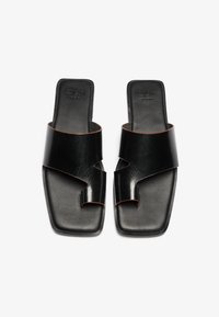 Sandales à glissière en cuir noir avec des brides croisées, bout carré, semelle texturée et subtile accent brun sur les bords.