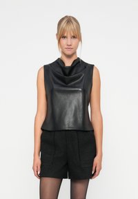 Top smanicato in pelle nera con design a collo alto, texture liscia e vestibilità comoda, abbinato a pantaloni corti neri con texture.