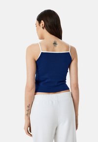 Marineblauw crop top met witte schouderbanden, gemaakt van een zachte brei-stof. Heeft een nauwsluitend ontwerp en subtiele textuur.