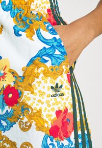 Adidas-shorts med ett färgglatt blommönster och ornamenterade dekorationer på vit bakgrund, med gröna ränder och logodetalj vid fållen.