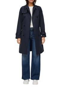 Granatowy płaszcz trench z podwójnym zapięciem, guzikami i pagonami na ramionach. W zestawieniu z dżinsami o szerokich nogawkach i białymi sneakersami.