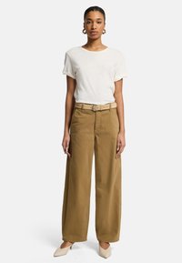 Camicia bianca a maniche corte abbinata a pantaloni beige a gamba larga e una cintura coordinata. L'outfit presenta una vestibilità comoda e un design minimalista.