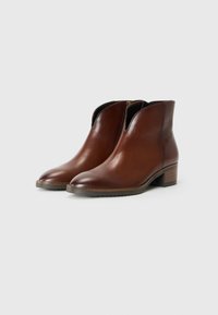 Bottines en cuir marron avec un bout pointu, des panneaux latéraux élastiques et un petit talon empilé. Texture lisse et design minimaliste.