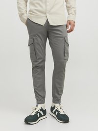 Grey cargo pants with elastic cuffs, side pockets, and a slim fit. Worn with dark green sneakers featuring white accents and laces.