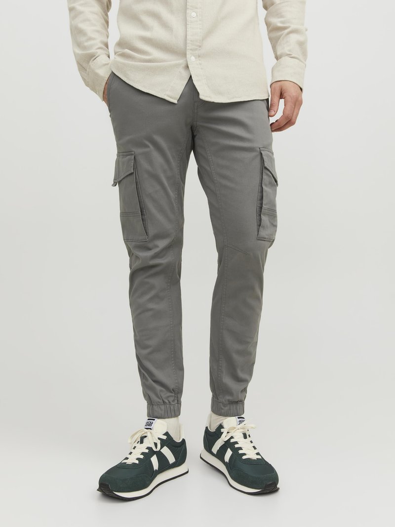 Grey cargo pants with elastic cuffs, side pockets, and a slim fit. Worn with dark green sneakers featuring white accents and laces.