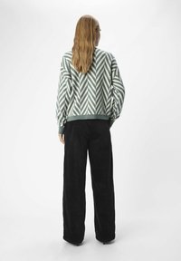 Suéter de gran tamaño de patrón zigzag en verde y blanco con dobladillo acanalado, combinado con pantalones de pana anchos en negro. Vista trasera.
