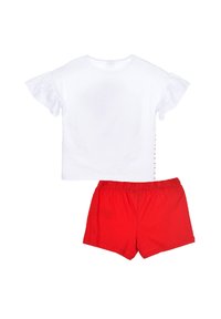 Camiseta blanca de algodón con mangas cortas y volantes, combinada con pantalones cortos rojos de algodón que tienen una cintura elástica.