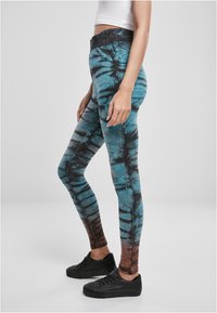 Tajta leggings med ett tie-dye-mönster i turkos och svart, med en mörkbrun övertoning vid vristen. Mjukt, elastiskt material.