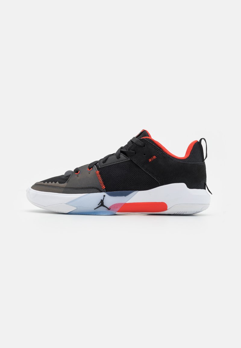 Chaussures de sport noires avec des accents rouges, en matériaux en maille et synthétiques, design basse, semelle en caoutchouc, et une marque distinctive sur le côté.
