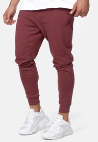 Burgundowe spodnie dresowe o tapered fit, z ribbrowymi mankietami i małym czarnym logo. W zestawieniu z białymi sneakersami z siateczkowymi i skórzanymi akcentami.
