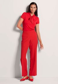 Rotes kurzärmeliges Oberteil mit einer Schleifendetail, kombiniert mit hochgeschnittenen, weit geschnittenen roten Hosen und passenden roten spitzen Flats.