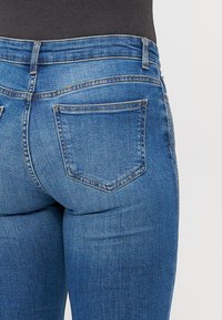 Modre jeans hlače iz denima s prilagojenim dizajnom, opremljene z dvema zadnjima žepoma, svetlobe bledenja in ojačanim šivanjem ob pasu.
