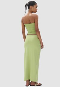 Lichtgroen twee-delig outfit met een aansluitend, strapless top en een lange, vloeiende rok. Glad textuur en naadloos ontwerp.