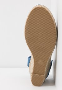 Semelle d'une espadrille beige avec des côtés en tissu bleu, affichant le numéro de taille quatre tamponné sur la zone du talon.