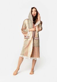 Kapucňový tkaný plášť v jemných odtieňoch zlatej, hrdzavej a sivej; obsahuje dve vrecká, strapcovú dolnú časť a texturované pruhy. Mäkkučká, ľahká tkanina.