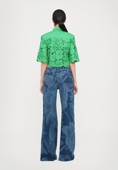 Green floral lace blouse with short sleeves paired with wide-leg dark blue jeans featuring tonal floral patterns and a classic five-pocket design.