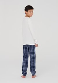 Biała koszula z długim rękawem połączona z granatowymi, w kratkę piżamowymi spodniami, o miękkiej teksturze i elastycznych mankietach, zaprojektowana z myślą o komforcie.