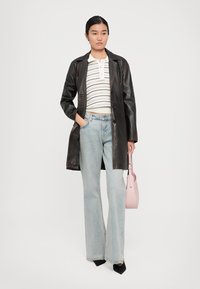 Donna che indossa un cappotto di pelle scura, una maglia a righe bianche, jeans azzurri chiari, tacchi neri e tiene in mano una borsa rosa chiaro.