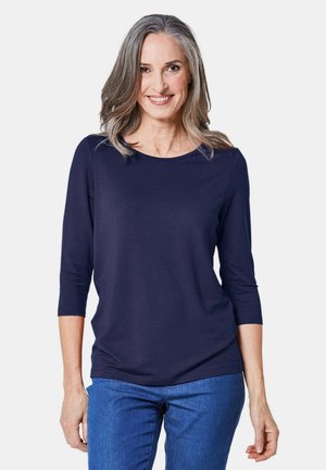 Navyblaues Oberteil mit dreiviertel Ärmeln aus weichem Stoff. Rundhalsausschnitt mit lockerer Passform. Getragen mit blauen Jeans.