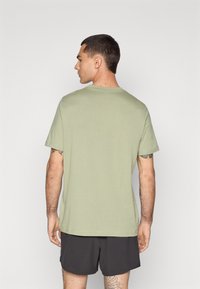 Lichtgroene t-shirt met korte mouwen, gemaakt van zacht stof, met een klassieke ronde hals en een ontspannen pasvorm, gecombineerd met donkere shorts.