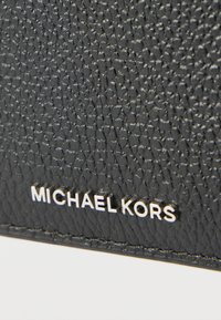 Schwarze Ledertasche mit strukturierter Oberfläche, geprägt mit Logo und silberfarbenen Akzenten, präsentiert ein kompaktes Design mit robuster Struktur.