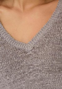 Pull à col en V en tricot gris clair avec un tissage lâche, présentant un tissu texturé et un léger éclat. Détail accentué au niveau de l'encolure.