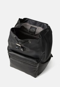 Sac à dos noir avec une surface texturée, un cordon de serrage et une poche zippée à l'avant. L'intérieur comprend une étiquette de marque.