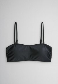 Musta saumaton bandeau-bikinitoppi ohuilla säädettävillä olkaimilla vaaleanharmaata taustaa vasten.