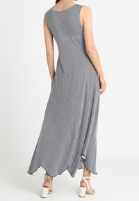 Długa sukienka w czarno-białe pionowe paski, bez rękawów, asymetryczny dół, wykonana z lekkiego materiału o gładkiej fakturze.