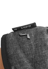 Tessuto nero testurizzato con un logo nero lucido in evidenza. Presenta l'etichetta R-Tex XT cucita nel bordo superiore. Forma rettangolare compatta.