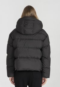 Czarna puchowa kurtka z wysokim kołnierzem i kapturem, z poziomym przeszyciem i prostokątnym krojem. Wykonana z gładkiego, ocieplanego materiału.