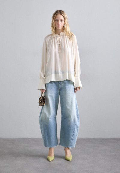 Blusa chiara in crema con maniche arricciate e dettaglio con coulisse, abbinata a jeans oversize azzurri, tacchi a punta gialli e una piccola borsa in stampa leopardata.