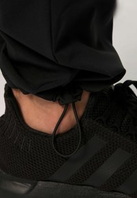 Zapatilla atlética negra con un upper de punto texturizado, diseño elegante y cordón elástico en el tobillo con acentos en negro mate.