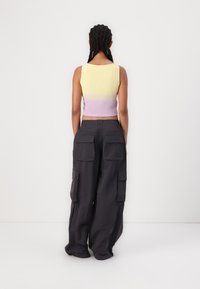 Žltý crop top s rebrovaným vzorom prechádzajúci do levanduľovej; kombinovaný s voľnými, tmavošedými cargo nohavicami s viacerými vreckami a uvoľneným strihom.