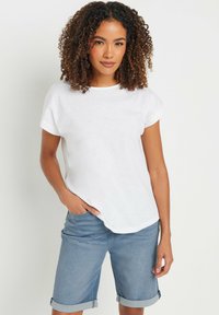 Camiseta blanca de manga corta con cuello redondo, hecha de tejido ligero. Combinada con pantalones cortos de mezclilla azul claros con el puño doblado.