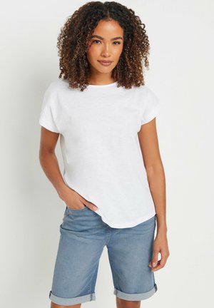 Witte T-shirt met korte mouwen en ronde hals, gemaakt van lichtgewicht stof. Gecombineerd met lichtblauwe denim shorts met opgerolde mouwen.