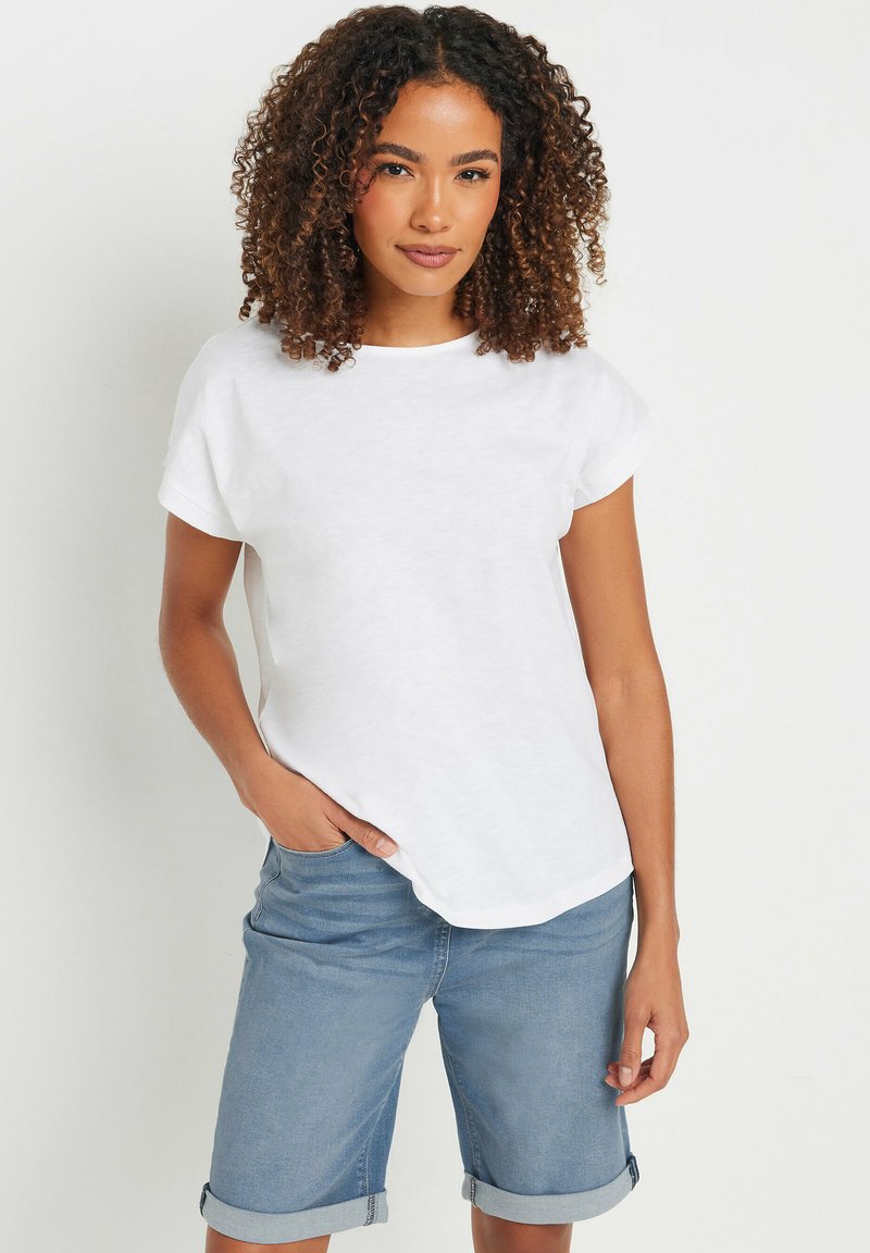 Camiseta blanca de manga corta con cuello redondo, hecha de tejido ligero. Combinada con pantalones cortos de mezclilla azul claros con el puño doblado.