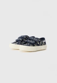 Sapatos de lona azul-marinho com padrões brancos em forma de concha, fechos de Velcro duplos e sola de borracha texturizada. Bico arredondado e design minimalista.