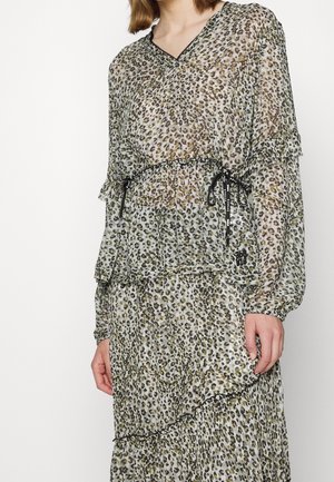 Kvinde iført en gennemsigtig, langærmet leopardprintkjole med sorte snor-detaljer i taljen og flæsekant.