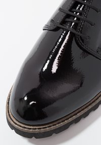 Gros plan sur l'avant d'une chaussure en cuir noir brillant avec des lacets noirs, des coutures visibles et une semelle robuste marron et noire.