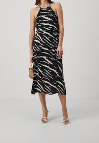 Sukienka w czarno-białym wzorze zebry z halterem, zwiewna sylwetka, lekki materiał i związany detal w talii. Połączona z białymi szpilkami.